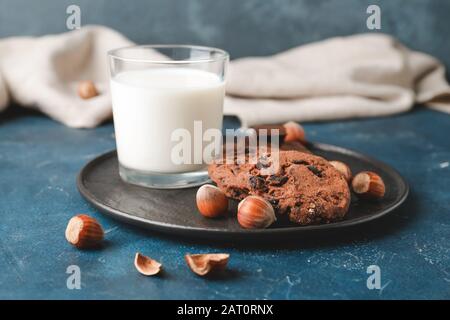 Tasty chocolate cookies with hazelnuts and glass of milk on dark background Stock Photo