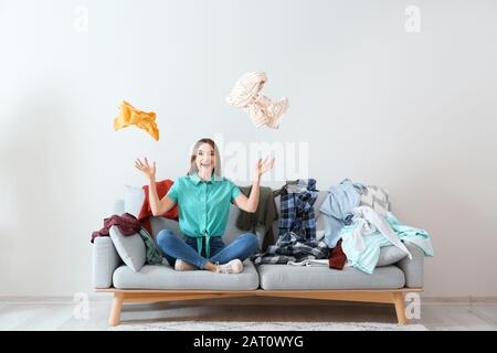 Young woman with heap of clothes on sofa indoors Stock Photo