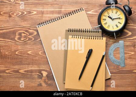 Stylish notebooks with alarm clock and stationery on wooden table Stock Photo