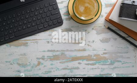 Overhead shot of rustic workplace with tablet, camera, office supplies, coffee cup and copy space on vintage table background Stock Photo