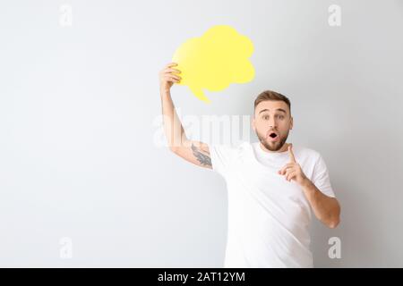 Surprised young man with blank speech bubble on light background Stock Photo