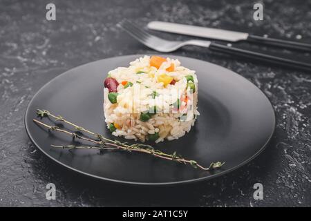 Plate with boiled rice and vegetables on dark background Stock Photo