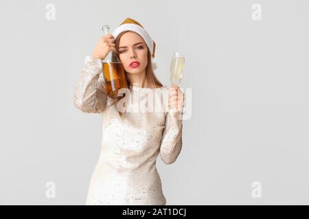 Drunk woman with Santa Claus hat and champagne on light background Stock Photo