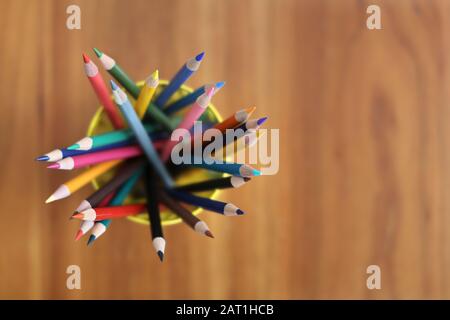 color pencils in yellow pencil holders on wooden table Stock Photo