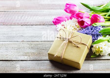 Bouquet of spring flowers hyacinth and tulips, and gift box on wooden table. Mother's Day or Woman Day Concept. Copy space Stock Photo