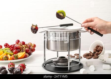 Woman dipping tasty fruits into bowl with chocolate fondue on table Stock Photo