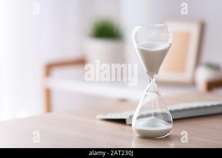 Hourglass with computer keyboard on table in office. Time management concept Stock Photo