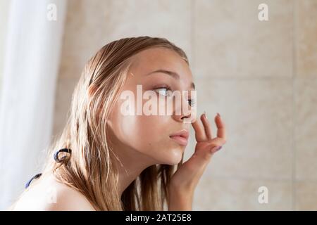 Young blond Caucasian girl does makeup in a bathroom Stock Photo