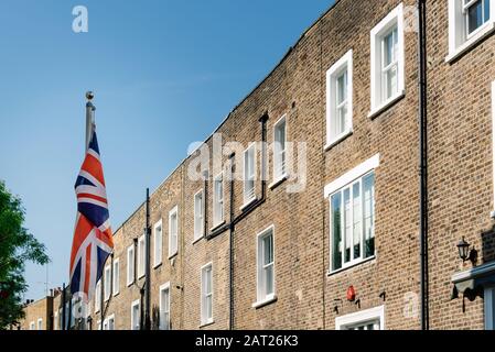 Union Jack british flag waving against typical red brick houses in London. Stock Photo