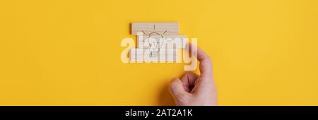 Wide view image of male hand assembling a light bulb drawing on wooden pegs in a conceptual image. Over yellow background. Stock Photo