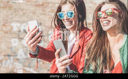 Happy fashion friends watching videos on smartphone - Girlfriends having fun social technology trends outdoors - Friendship, youth lifestyle, millenni Stock Photo