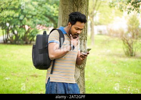 University indian student using mobile phone outdoor Portrait of a young Indian man texting in park residential contest - New technology trend addicti Stock Photo