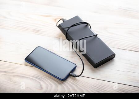 Smartphone charging via usb cable from black powerbank on wooden table. Stock Photo