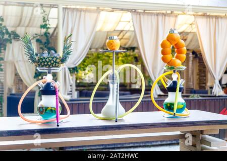 Three hookahs stand on the table in the cafe. Hookah on a pineapple hookah on the orange, Shisha on the milk. Round hookah flasks with blue liquid. Or Stock Photo