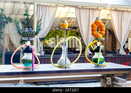 Three hookahs stand on the table in the cafe. Hookah on a pineapple hookah on the orange, Shisha on the milk. Round hookah flasks with blue liquid. Or Stock Photo
