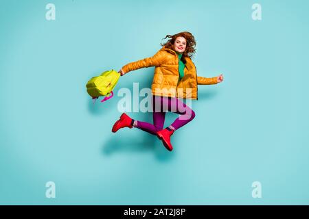 I'm free. Full size photo of funny lady jump high rush home after lessons classes carry school bag wear yellow coat scarf trousers turtleneck boots Stock Photo