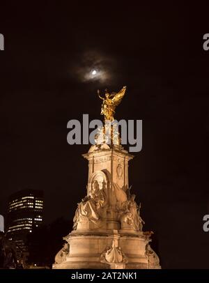 Low angle night view, Queen Victoria memorial statue by Buckingham Palace lit up, isolated in dark sky; Winged Victory statue shining in moon light. Stock Photo