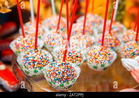 Delicious cake pops, sprinkled with colorful balls, lie on a glass stand. Stock Photo