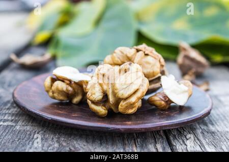 Walnuts and walnut kernels lie on a bowl on a rustic old wooden table. Walnut kernels. Harvest walnuts. Stock Photo