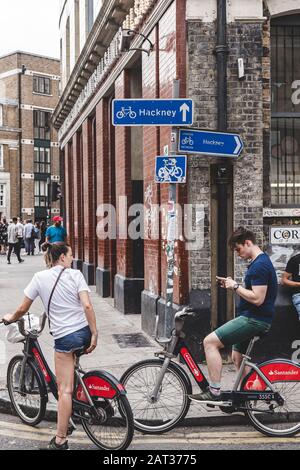 London/UK - 22/07/18: couple on Santander Cycles on a street checking their route via smartphone. Public bike share is a service in which bikes are ma Stock Photo