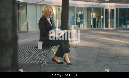 Side view of elegant businesswoman sitting on bench in patio and writing in notepad while working. Stock Photo