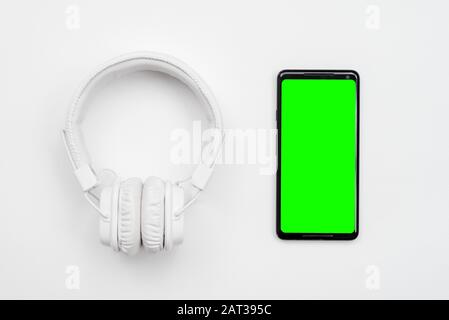 White wireless headphones and smartphone with green screen isolated on a white background. Stock Photo
