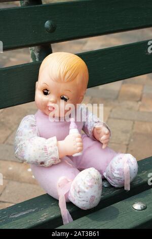 Closeup shot of a blinking eyes doll holding a feeding bottle and seated on a green bench Stock Photo Alamy