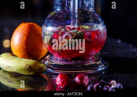 round hookah flask with red liquor. Sliced grapefruit and mint leaves float in the liquor. Lots of smoke Stock Photo