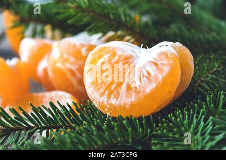 Ripe peeled slices of tangerine without peel lie on the green branches of a Christmas tree. Citrus fruits, tangerines or oranges. Close-up. Stock Photo