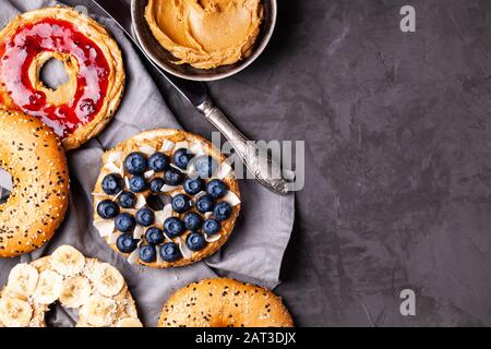 Variety of bagels with different toppings and natural paleo nut peanut cashew creamy butter on dark gray background.Healthy breakfast brunch concept Stock Photo