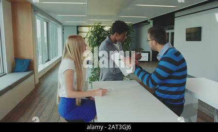 Group of diverse woman and men with tablet in modern office hall having work with documents and statistics Stock Photo