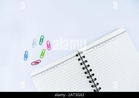 A white notebook along side some different colored paper clips on an isolated white background Stock Photo