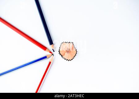 Four different colored wood pencils pointing towards a pencil shaving from different directions on an isolated white background Stock Photo