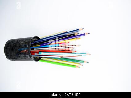 Various types of pencils and wax crayons placed in a jar which have fallen on an isolated white desk Stock Photo