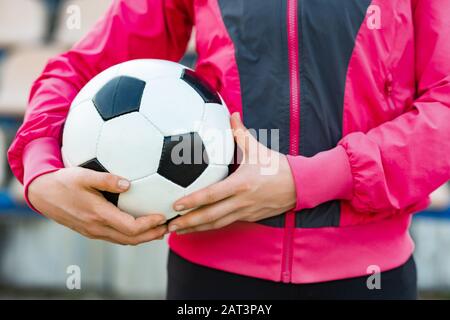 Adult's hands holding  football ball. Man or woman wearing sportwear - Image Stock Photo