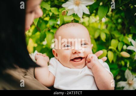 Beautiful portrait of little baby boy on flowers bush background. Child in spring blossom. Cute newborn son smiling. Stock Photo