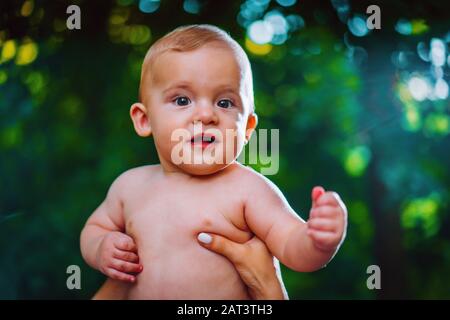 Handsome baby boy looking to camera and smiling on green forest background. Stock Photo
