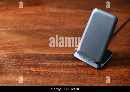 wireless charging stand for modern smartphones on wooden table. Stock Photo