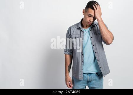 Portrait of a lamentable sad, mulatto man standing with his head down and touching his head with his hand Stock Photo