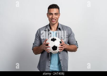 Half-length portrait a handsome mulatto man holding a football ball in his hands standing against a white wall Stock Photo