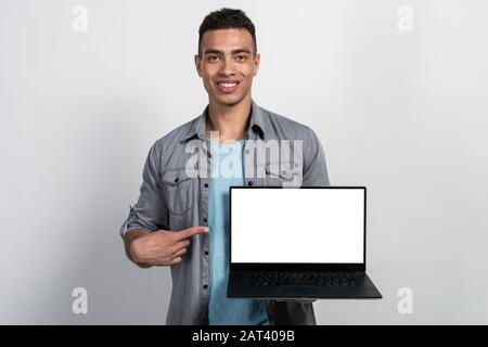 Happy mulatto man holding a laptop in his hands and pointing by index finger on screen . - Image Stock Photo