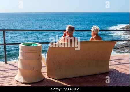 CANARY ISLAND TENERIFE, SPAIN - 27 DEC, 2019: A retired couple is sitting on a bench enjoying the sun and view on Tenerife. Stock Photo