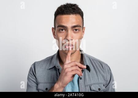 Man  saying hush be quiet with finger on lips gesture on white wall background closeup  - Image Stock Photo