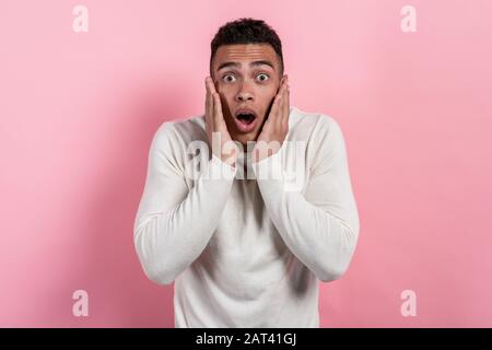 Surprised pretty man with open mouth posing in the studio against a pink background looking at the camera.- Image Stock Photo