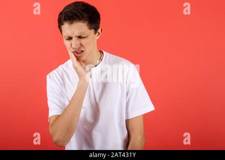 Young man feeling pain, holding his cheek with one hand, suffering from bad toothache Stock Photo