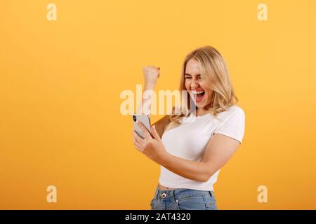 Young, beautiful, smiling girl looks at the phone and makes a winner gesture Stock Photo