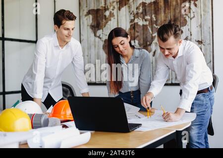 Two architects and young woman working at architect office with blueprints Stock Photo