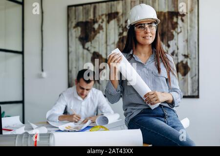 Young female architect in glasses and helmet architect works in office together with colleague Stock Photo