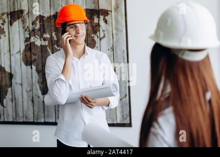 Handsome young successful business man in orange helmet holds drawing and speaks on mobile phone Stock Photo
