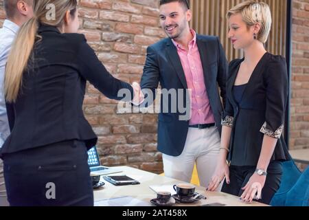 Business partners shake hands, standing in front of their office. Welcome to our team! Business people shaking hands while working in the creative off Stock Photo
